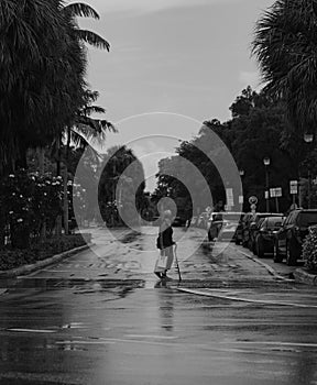 Grayscale of a woman crossing a wet city street on a rainy day