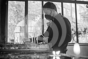 Grayscale of a young man praying and lighting candles in a church, Yerevan, Armenia