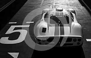 A graysilver race car with a front spoiler and rear wing, displayed in an indoor setting likely garage or paddock, positioned at