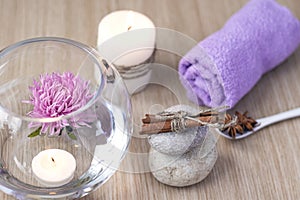 Graystones on top of each other, a candle, a lilac rolled towel, a vase of water with a lilac flower and candles floating in the