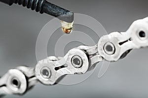 Greasing a bicycle chain with a drop of golden oil close-up on a gray background