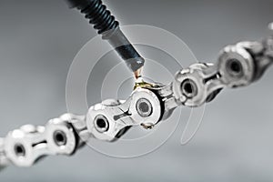 Greasing a bicycle chain with a drop of golden oil close-up on a gray background