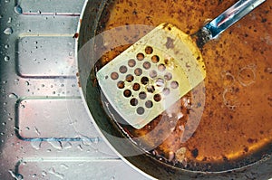 Greasy steel pan and perforated spatula on steel sink with water droplets