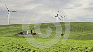 Great abandoned farmhouse surrounded by rolling green hills covered with grass and wind generators of electricity