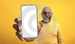 Great app. African american senior man showing big empty cellphone screen, recommending your ad, mockup photo