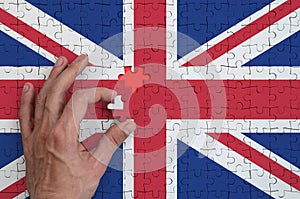 Great britain flag is depicted on a puzzle, which the man`s hand completes to fold