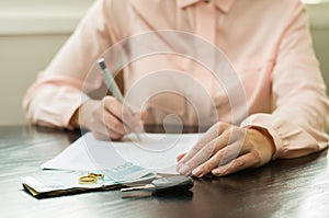 Great concept of divorce, end of relationship, young woman signing divorce agreement. Money, car key on the table