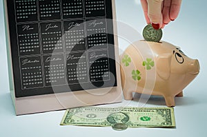 Great concept of economy, calendar, piggy bank, american dollar money notes. Woman hand inserting coin into the piggy bank