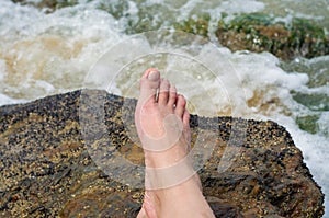 Great concept of relaxation, woman legs on the stone on the beach