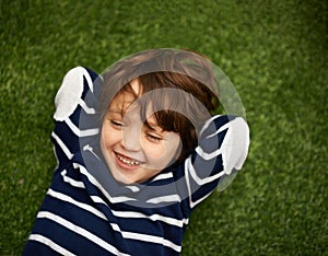 Great giggles. Little boy lying on the grass with his hands behind his head.
