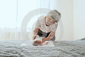 Great-grandmother plays with a newborn great-granddaughter. The baby lies in the arms of the grandmother