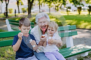 Great grandmother sitting on bench with her grandchildren and blowing soap bubbles together, generation family concept.