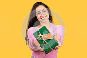 Great idea for present. Positive young arab woman giving box with present isolated on yellow background