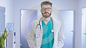 Great looking guy doctor in a modern hospital corridor with a eyeglasses looking straight to the camera concentrated he