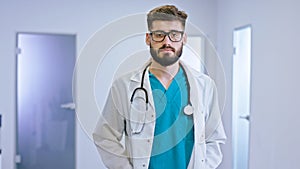 Great looking guy doctor in a modern hospital corridor with a eyeglasses looking straight to the camera concentrated he