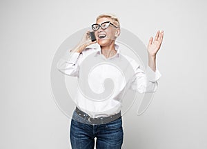 Great news. Modern Communication. Happy senior woman using mobile phone over grey background.