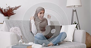 Great news online. Joyful arabic woman looking at laptop screen screaming and raising hands with excitement