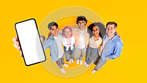 Great offer. Excited multiracial friends showing smartphone with empty screen, mockup, panorama, above view