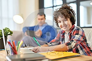 Great place to learn. Cheerful hispanic school boy wearing headphones, smiling at camera while preparing homework