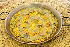 Great and popular Valencian rice paella presented in a paella pan with green flat beans, chunks of stewed chicken, white garrafon photo