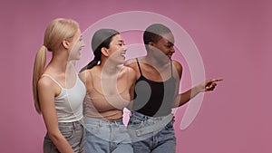 Great shopping promo. Three diverse women looking aside and laughing at empty space, smiling to camera, pink background