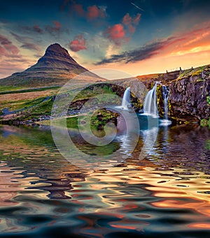 Great sunrise on Kirkjufellsfoss Waterfall reflected in calm waters of Atlantic ocean.