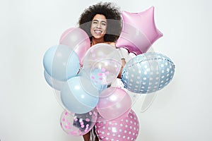 Great surprise! Happy and beautiful afro american woman holding a bunch of colourful balloons and looking at camera with