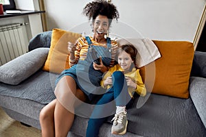 Great time. African american woman, baby sitter and caucasian cute little girl having fun together, playing video games