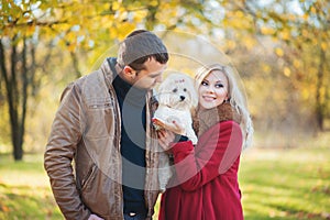 Great time for walk! Beautiful family couple with white cute Maltese dog spending time in autumn park