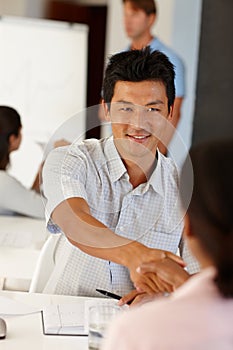 Great to meet his new partner. an asian man shaking hands with a coworker in a work seminar.