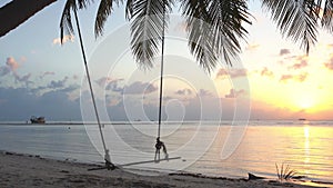 Great tropical beach. Sunset, a swing sways on a palm tree. Calmness and comfort. 4k video.