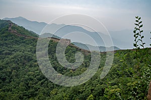 Great view from Great Wall of China with a green trees and rocky mountains in the background. Misty foggy air above the hill