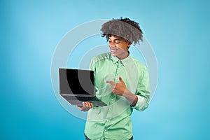 Great website. Teen african american guy showing laptop computer blank screen, standing over blue background