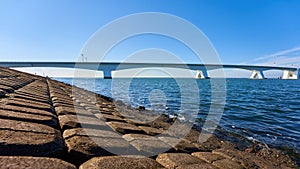 Great Zeeland Bridge, dam made of stone blocks, deep blue sea water and cloudless sky. Netherlands