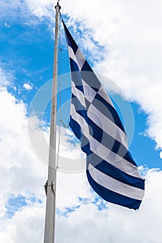 Greece flag fluttering on mast against background of saturated blue sky with white clouds