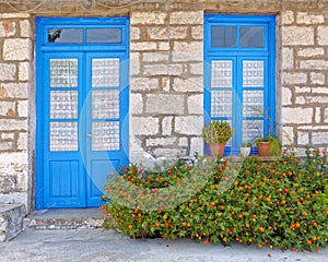 Greece, marigold flowers in front of blue door and window, house facade