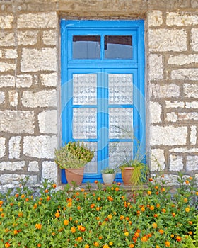 Greece, stone wall house blue window and marigold flowers
