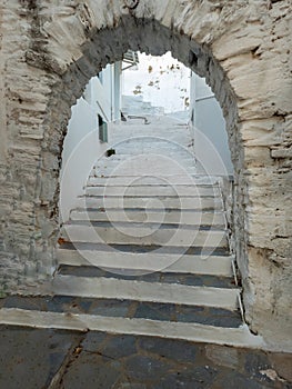 Greece, Tinos island, Cyclades. Arched stonewall entrance in front of stone paved stairs. Vertical