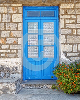 Greece, blue door on traditional island house stone wall and marigold flower