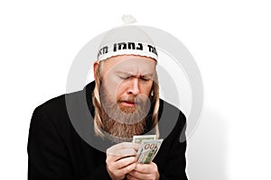 Greedy bearded jewish man counting his money. Thrifty jew with sidelocks in white yarmulke isolated on white background