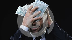 Greedy business man stroking face with dollars banknotes, enjoying wealth