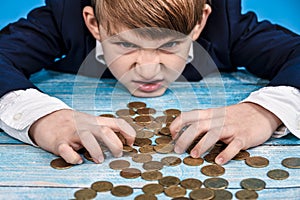 The greedy and greedy child covered the coins with his hands and looks around angrily