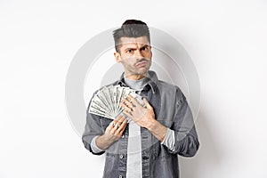 Greedy guy frowning and hugging dollar bills, unwilling to share money, standing on white background