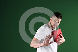 Greedy man hiding gift box on green background, space for text