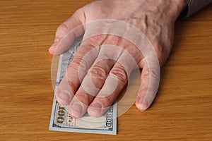 Greedy man`s hand takes a bribe of a one hundred us dollars banknote over a wooden table