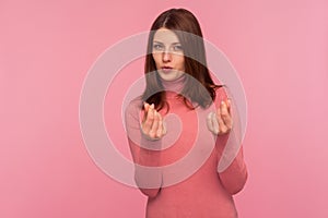 Greedy mercantile woman with brown hair in pink sweater asking cash showing money gesture with fingers seriously looking at camera