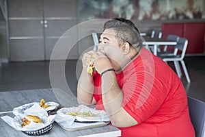 Greedy obese man eating fast foods in restaurant