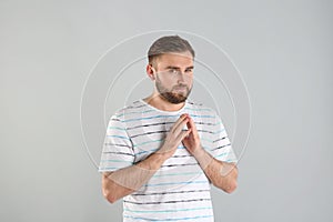 Greedy young man rubbing hands on light grey background