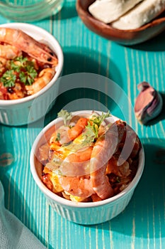 Greek appetizer, Saganaki. Shrimp baked with vegetables and cheese,on a blue wooden background, with hard shadows. Close