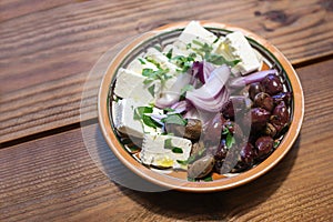 Greek appetizer snacks, herb olives, onions and feta cheese in a ceramic bowl on a rustic wooden table, copy space, selected focus